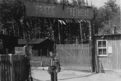 a man from Poland stands below a gate erected in camp by freed men. si